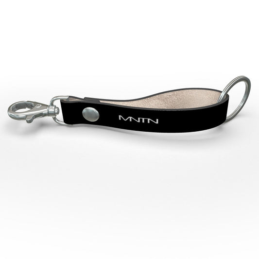 Angled view of the black leather key strap with a white MNTN logo, silver-tone hardware and the plain inner loop visible